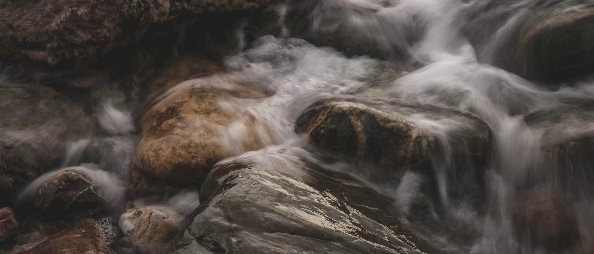 Water flowing over smooth dark rocks in a stream.
